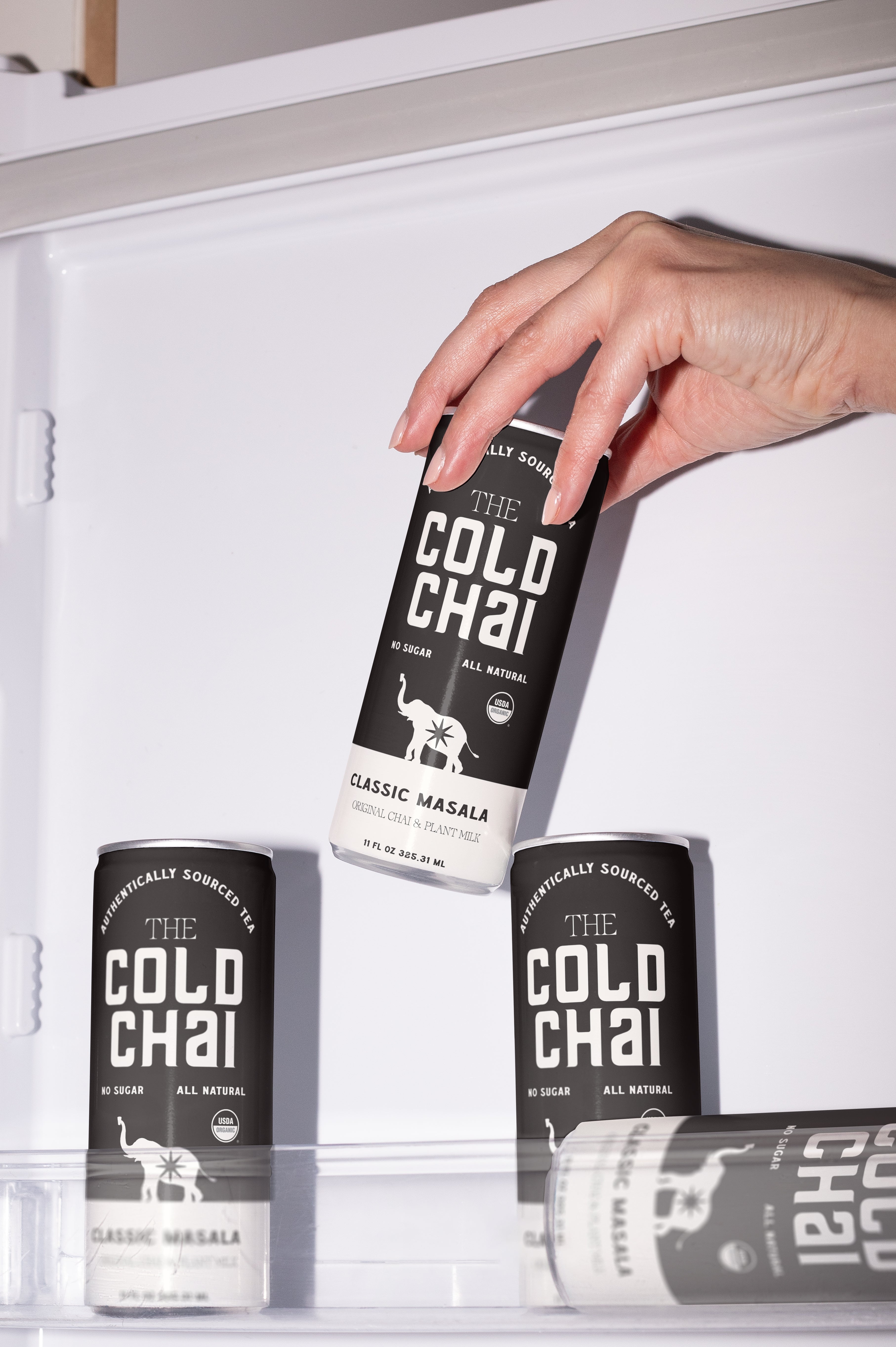 Hand reaching for a can of 'The Cold Chai' in an open refrigerator.